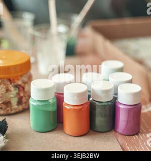 Colorful variety of craft paint bottles on table with glitter and brushes for art projects Stock Photo