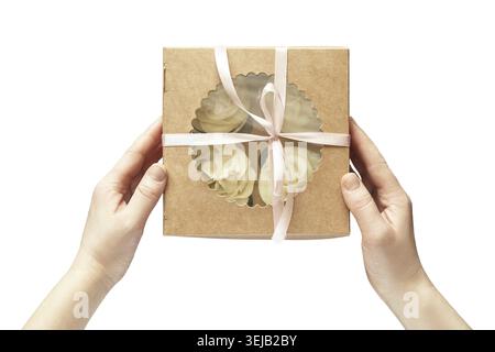 Caucasian female hands holding brown box with white cupcakes tied with pink ribbon on black background Stock Photo