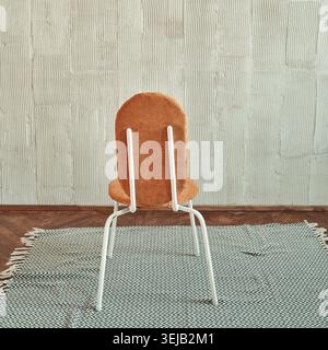 Modern orange chair with white frame on patterned rug in minimalist room with textured walls Stock Photo