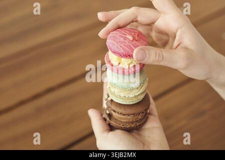 Stack of colorful macarons held by caucasian female on wooden table background Stock Photo