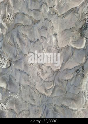 A top down view of natural grey sand ripples created by water flow at a river bank. The textures highlight the movement of water over time, displaying Stock Photo