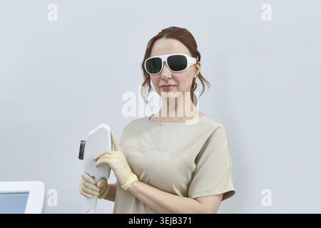 Caucasian young adult female laser technician holding equipment in professional medical setting Stock Photo