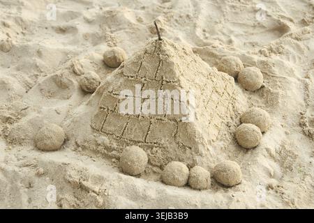 Sand pyramid on beach surrounded by spherical sand sculptures in sunlit setting Stock Photo