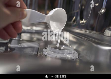 Hand pouring dishwasher salt into dispenser inside open dishwasher close up Stock Photo