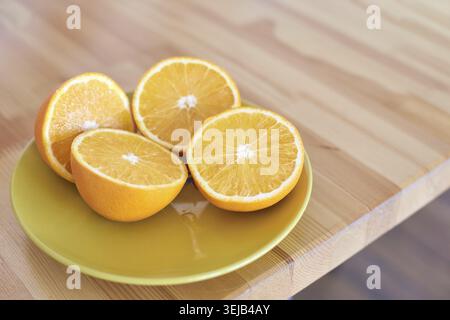 Fresh orange halves on yellow plate resting on wooden table surface in bright natural light Stock Photo