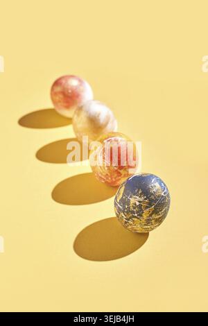 Colorful marbled balls in warm tones on yellow background casting shadows in artistic composition Stock Photo
