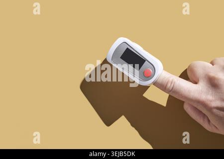 Adult hand using fingertip pulse oximeter on finger against plain background Stock Photo