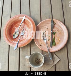 Empty plates and coffee cup on wooden table after meal with cutlery and napkin Stock Photo