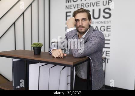 Thoughtful businessman stands leaning on a shelf with folders for documents in the office Stock Photo