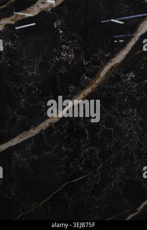 A polished black marble surface showcases beautiful gold and white veining, creating a luxurious texture perfect for countertops, flooring, or decorat Stock Photo