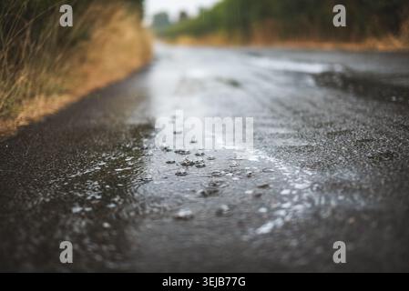 The surface of a dark, wet asphalt road is shown with numerous small raindrops creating ripples and splashes on its surface Stock Photo