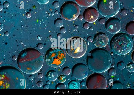 Detailed macro photograph of oil bubbles forming circular abstract patterns on a textured surface. Metallic blue and orange reflections create a futur Stock Photo