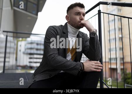Portrait of a thoughtful young man sitting on the steps next to his own building Stock Photo