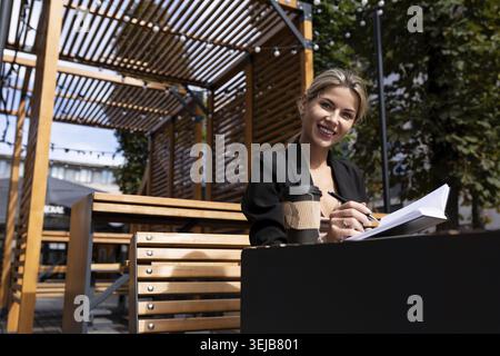 Successful businesswoman working outdoors drinking coffee and making notes in her diary Stock Photo