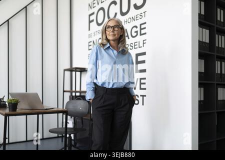 Business woman executive in a blue shirt stands in the middle of the office and looks into the distance Stock Photo