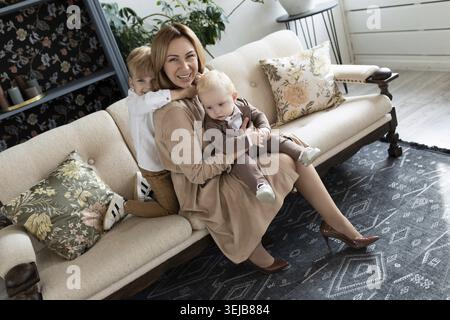Happy mom fooling around with two boys sons sitting on sofa Stock Photo
