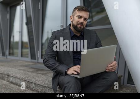Business man with laptop sitting on the steps of an office building Stock Photo