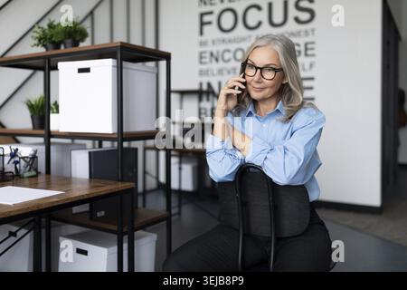 Business gray-haired fifty year old woman talking on the phone in the office Stock Photo