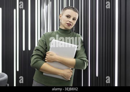 Woman programmer with a laptop in her hands against the background of a wall in the office Stock Photo