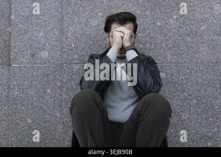 Grieving man sitting upset covering his face with his hands Stock Photo