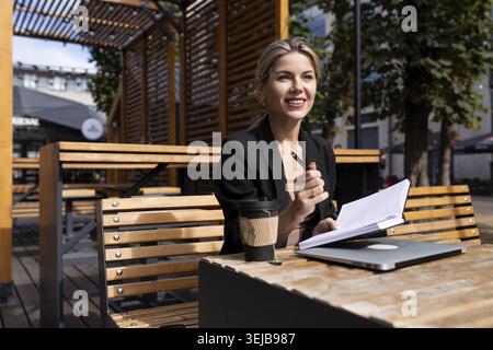 Young woman specialist works outdoors with a laptop and makes notes in a diary Stock Photo