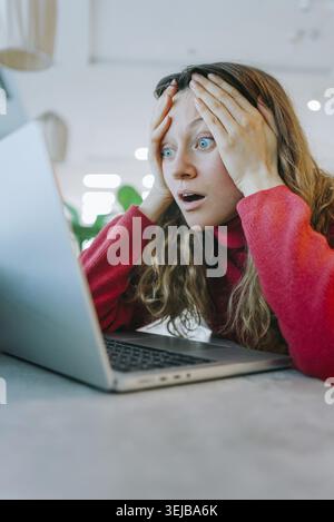 Stressed woman with head in hands, staring at laptop screen while receiving bad news about a cyber attack or system error Stock Photo