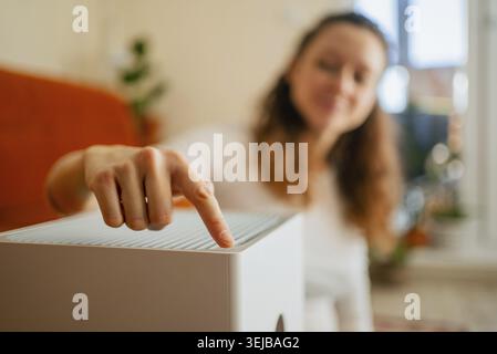 Woman's hand pressing a button on a contemporary white air purifier, adjusting settings to improve indoor air quality and promote a healthier living s Stock Photo
