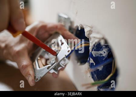 Electrician uses a screwdriver to carefully install a new electrical outlet in a wall, connecting wires and ensuring safety during home renovation Stock Photo