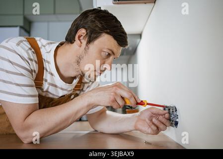 Electrician installing electrical sockets in a kitchen, using a screwdriver to secure connections and ensure functionality, highlighting expertise in Stock Photo