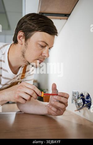 Electrician is carefully installing electrical sockets in a contemporary kitchen, utilizing a screwdriver with precision and expertise to ensure prope Stock Photo