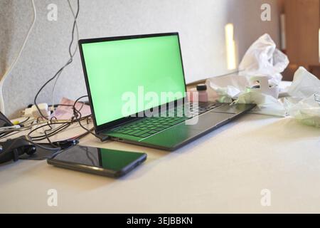 Laptop And Smartphone With Green Screens On Cluttered Desk In Modern Workspace Environment Stock Photo