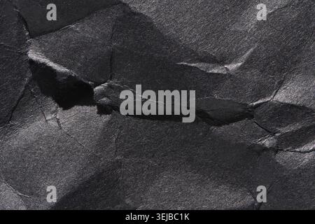 Textured black crumpled paper with shadows and highlights displaying rough surface details Stock Photo