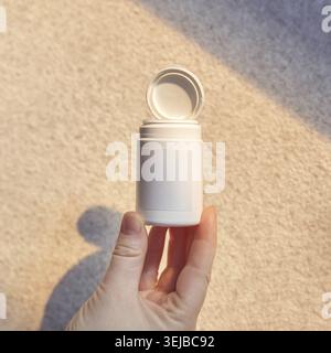 Female hand holding open white container with blank label on beige background in soft light Stock Photo