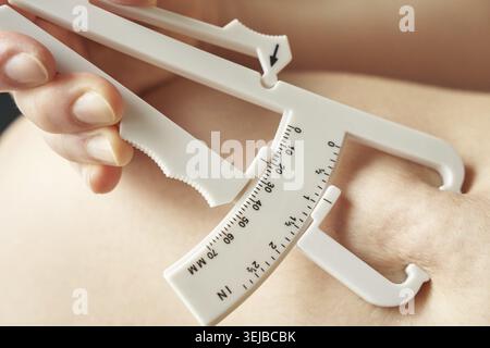 Female using skinfold caliper for body fat measurement, close-up of caucasian hand and caliper on skin Stock Photo