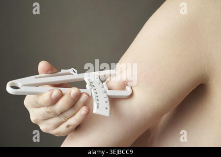 Female hands using skinfold caliper for body fat measurement on arm close-up Stock Photo