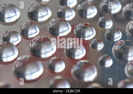 Close-up of reflective water droplets on smooth surface capturing light and colorful abstract reflections Stock Photo