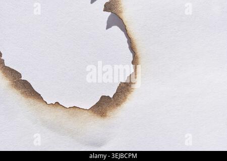 Close-up of burnt torn hole in white paper with scorched edges exposing a cutout Stock Photo