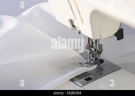Tailoring Process on Sewing Machine with White Cloth. Macro shot of a sewing machine in action with white cloth under the needle Stock Photo