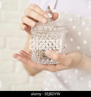 Female hands holding a decorative glass jar with diamond pattern in soft pastel setting Stock Photo