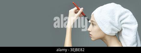 Young caucasian female applying makeup with brush wearing towel on head side profile Stock Photo