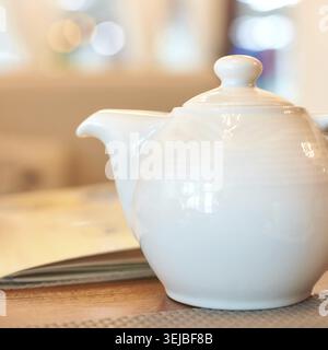 Elegant white ceramic teapot on wooden table in cozy cafe setting with soft ambient lighting Stock Photo