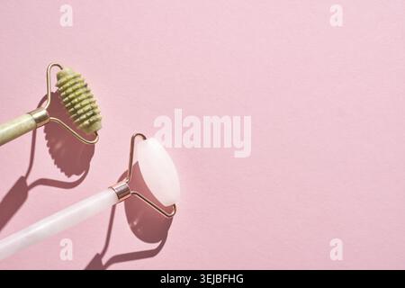 Jade and rose quartz facial rollers on pink background for skincare routine Stock Photo