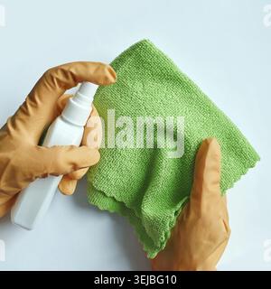 Hands wearing orange gloves cleaning with spray bottle and green microfiber cloth on light blue background Stock Photo