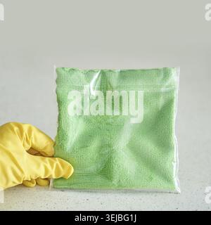 Hand holding green cleaning cloth in plastic bag on gray surface with yellow glove Stock Photo