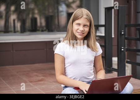 Caucasian young female student with laptop sitting outdoors smiling Stock Photo