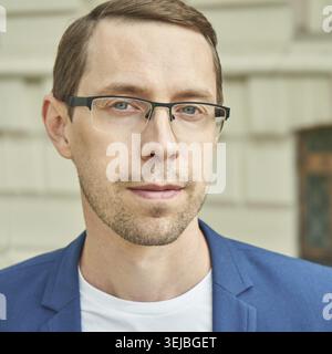 Young caucasian male in blue blazer and glasses standing outdoors near historic building Stock Photo