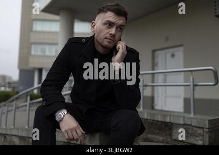 Stylish brutal man in a black coat on the background of the city Stock Photo