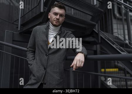 Stylish young caucasian he man in autumn coat on black stairs outside Stock Photo