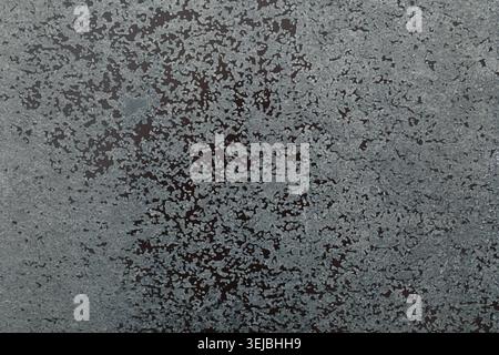 A textured surface displays a mix of gray particles on a dark backdrop, highlighting a unique abstract pattern formed by natural elements and time Stock Photo