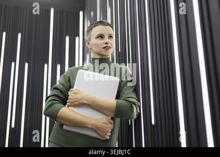 Mature woman website developer with a laptop in her hands against a black wall Stock Photo